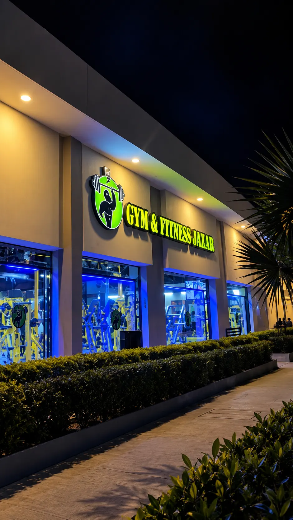 Fachada nocturna de Gym & Fitness Jazar en Plaza Vía Gavia, Villa Sur, con el letrero iluminado