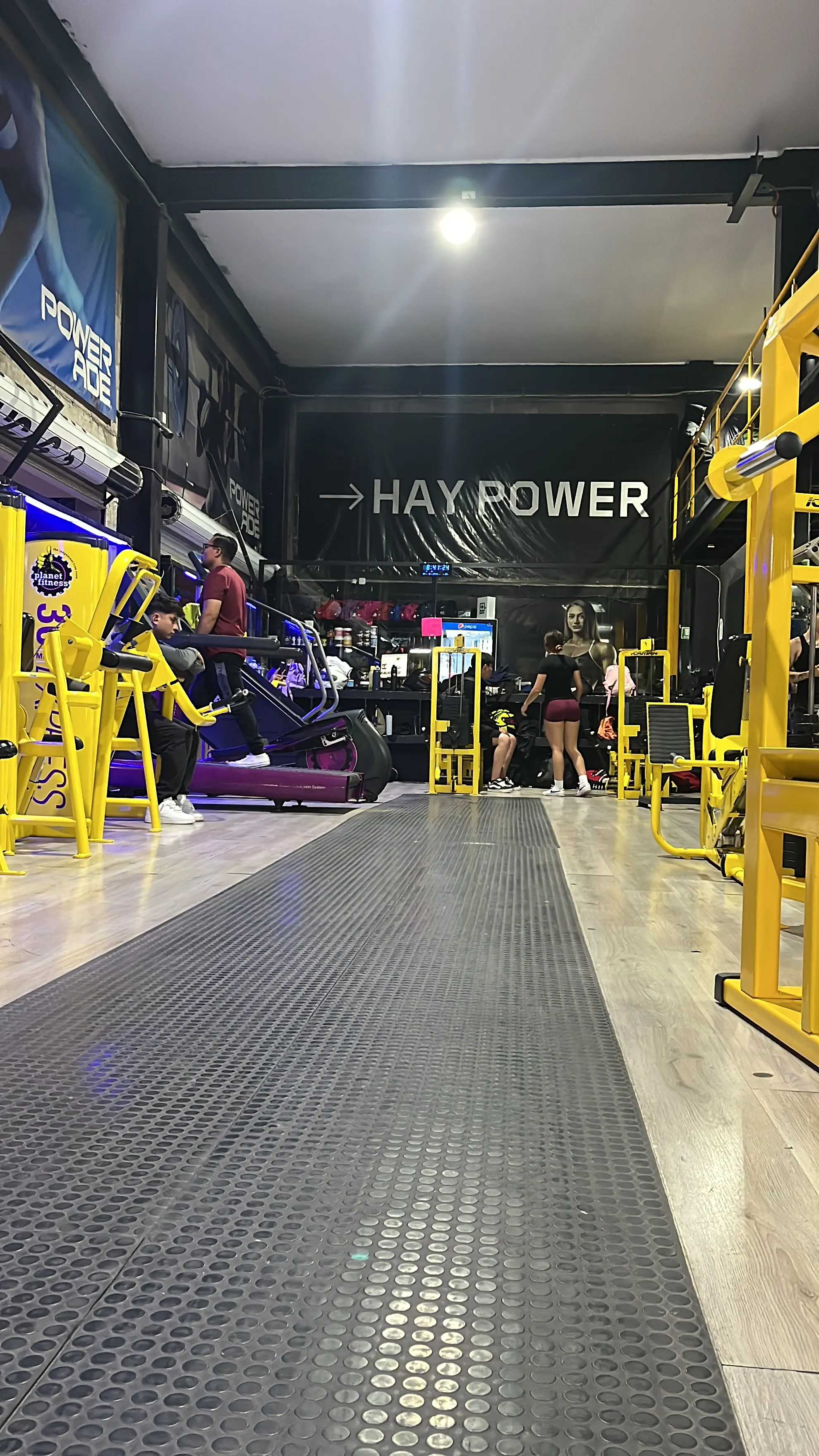 Pasillo central de Gym & Fitness Jazar con el letrero Hay Power, caminadora y máquinas amarillas