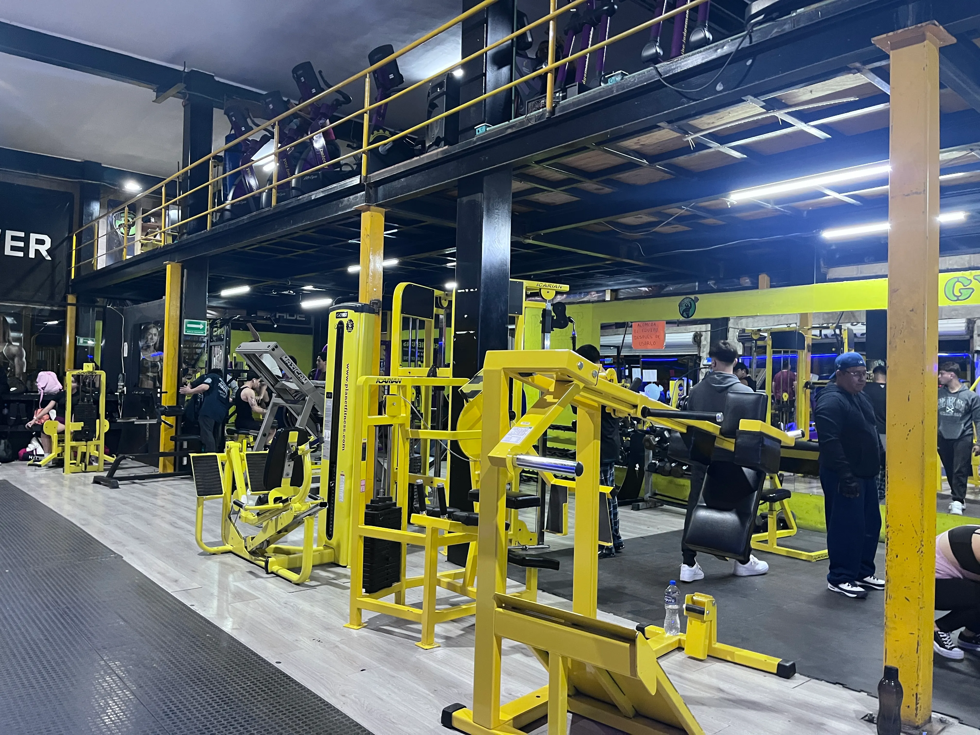 Piso de máquinas amarillas y gente entrenando en el área de dos niveles de Gym & Fitness Jazar, Villa Sur