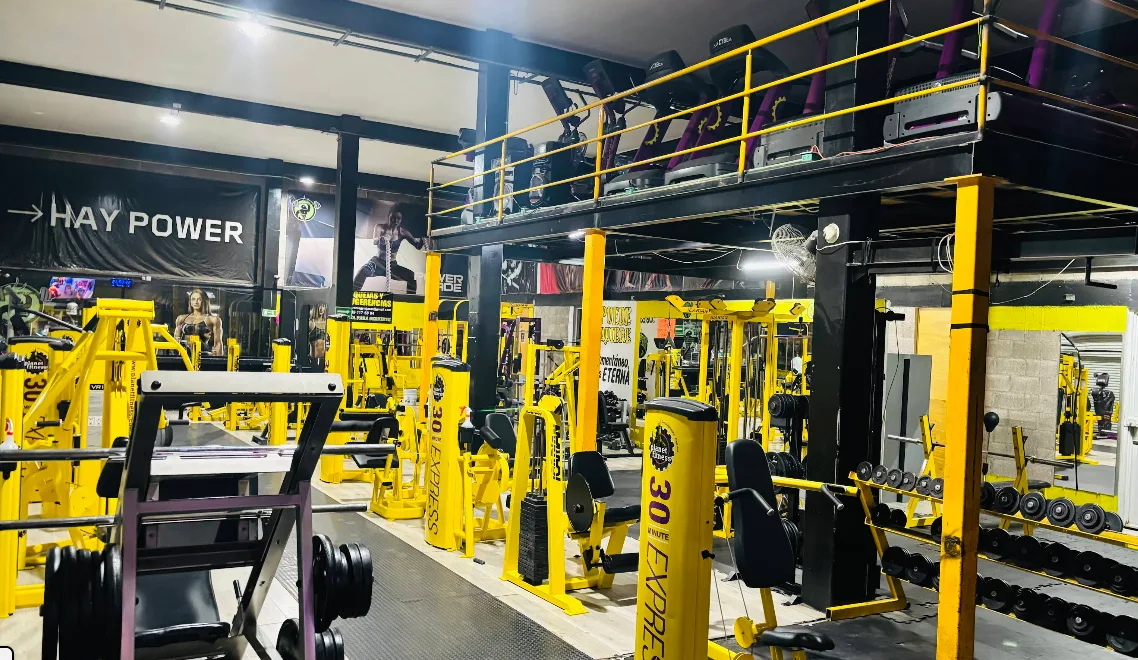 Interior de dos niveles de Gym & Fitness Jazar en Villa Sur, Aguascalientes, con máquinas y barandales amarillos